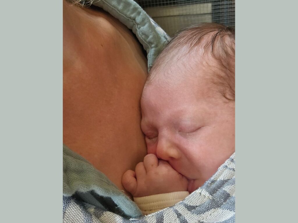 Newborn sucking thumb in carrier