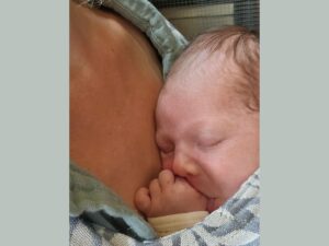 Newborn sucking thumb in carrier
